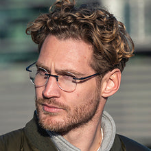 Load image into Gallery viewer, Close Up of Man with Scojo Round Gels glasses. He has a beard and is looking to the side with a blurred background