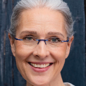 Female Model leaning against a barn wearing Gels reading glasses Cobalt color 735